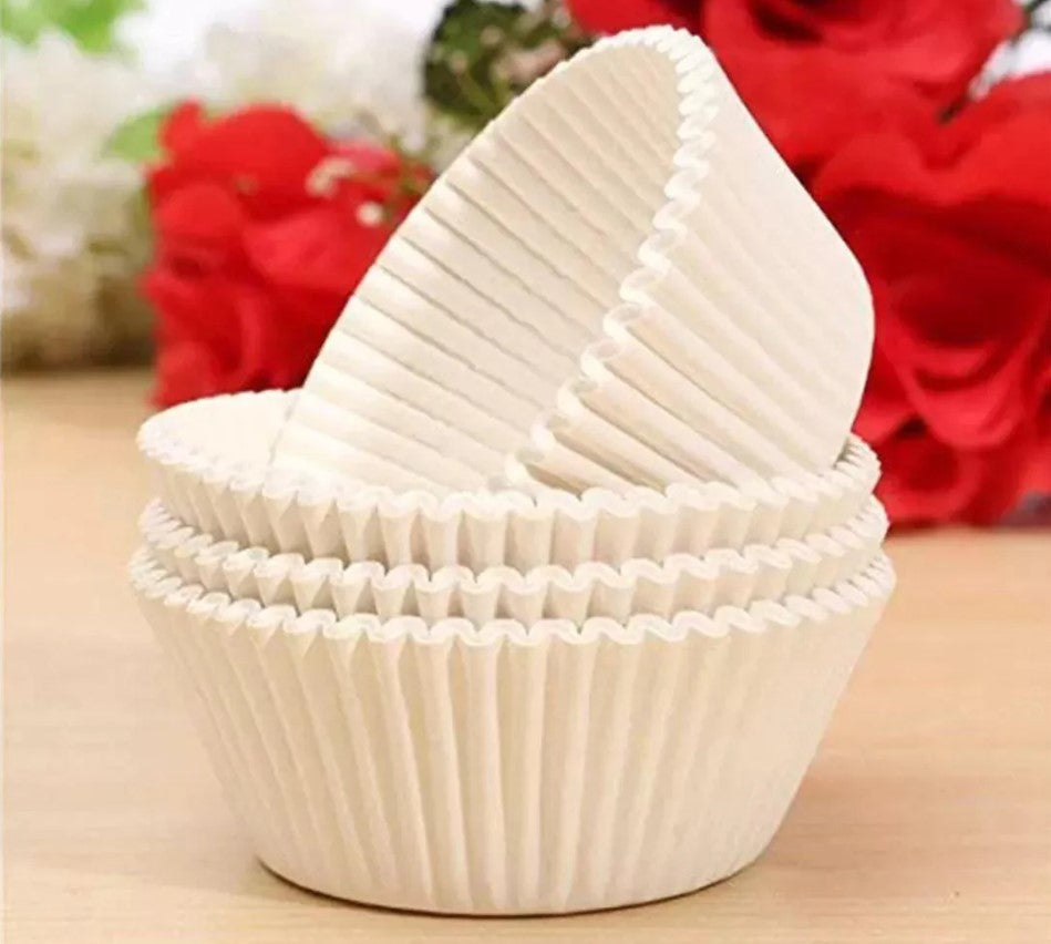 White cupcake liners on a wooden surface with red flowers in the background
