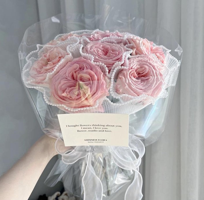 Bouquet of pink roses with a decorative wrap and card held by a person.