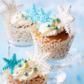 A set of three snowflake-patterned plunger cake cutters in varying sizes, with the smallest in blue, the medium in white, and the largest in silver, displayed against a blue textured background.