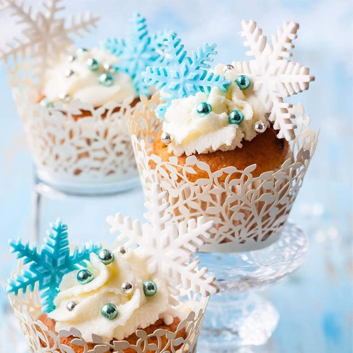 A set of three snowflake-patterned plunger cake cutters in varying sizes, with the smallest in blue, the medium in white, and the largest in silver, displayed against a blue textured background.