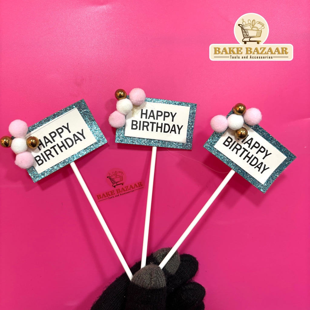 Three 'Happy Birthday' cake toppers with decorative sticks on a pink background, featuring the Bake Bazaar brand.