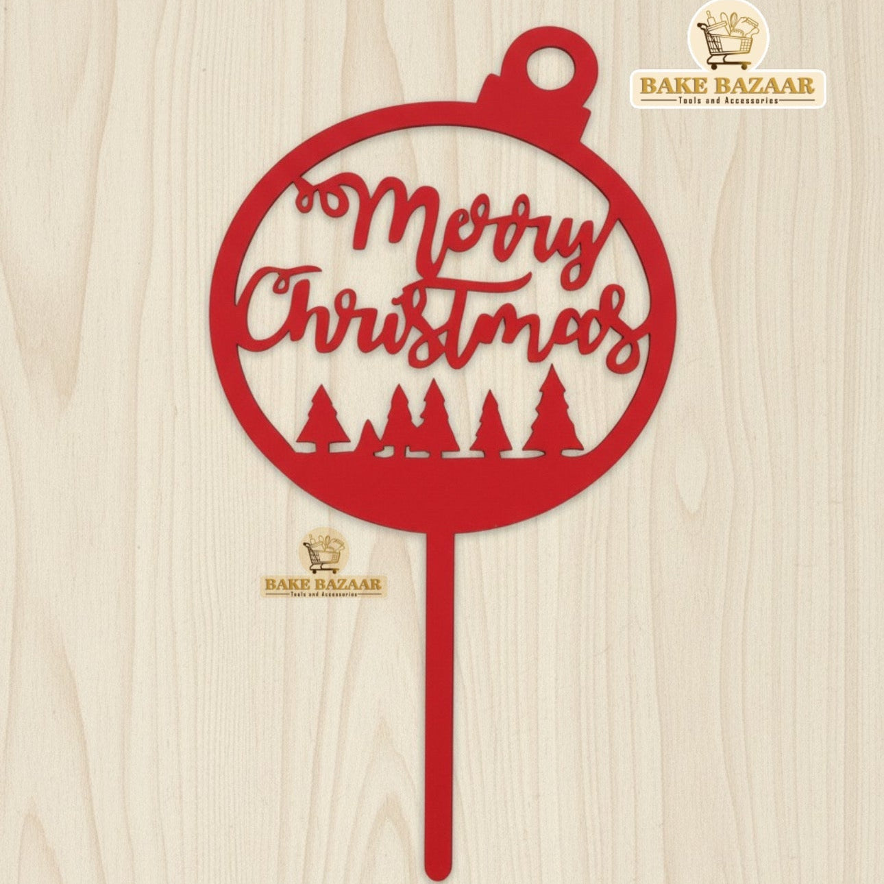 Red 'Merry Christmas' decoration with trees on a wooden background, branded 'Bake Bazaar'.