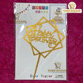 Gold 'Happy Birthday' cake topper packaging on a pink background