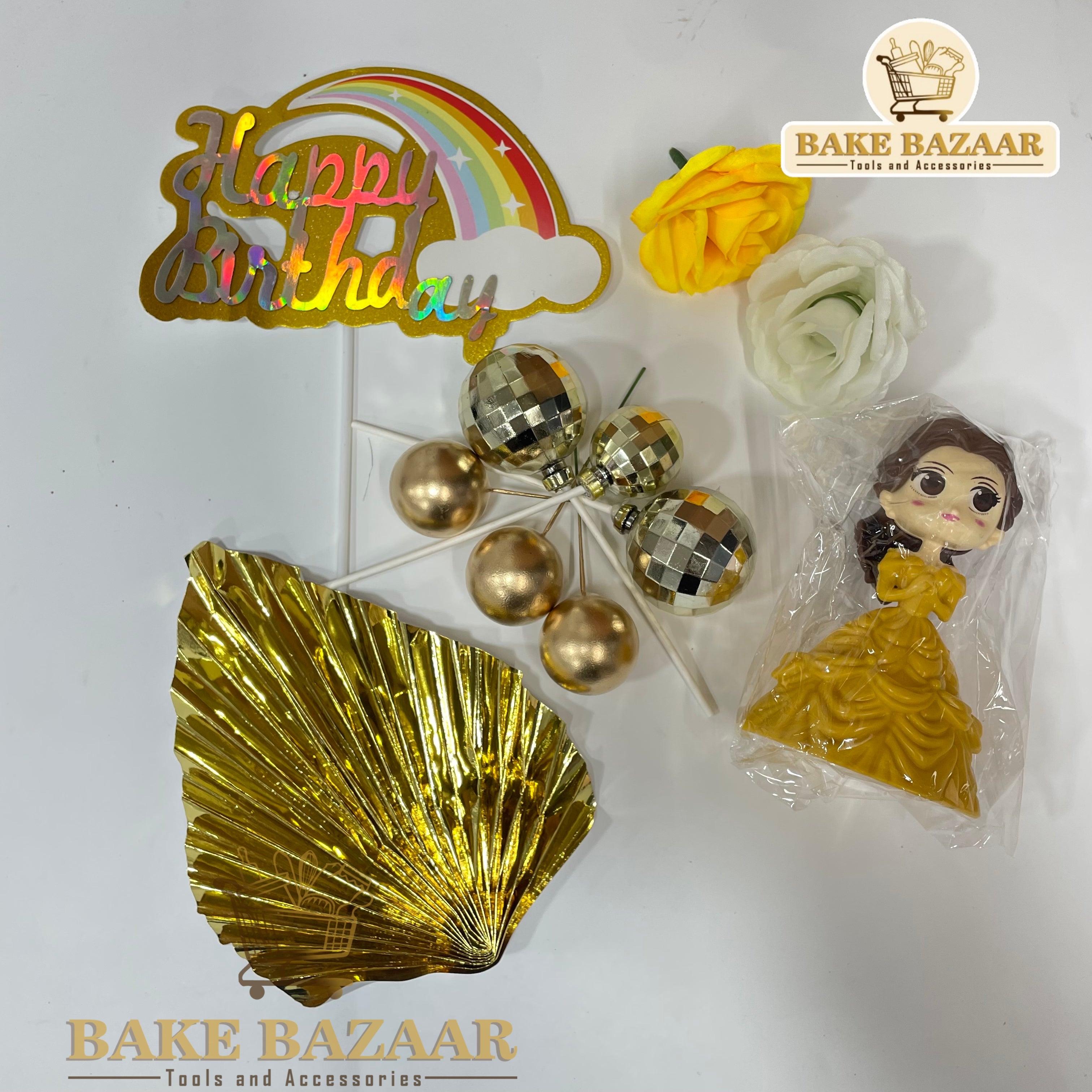 Decorative items including a 'Happy Birthday' cake topper, gold shell, flowers, and a figurine on a white background with 'Bake Bazaar' branding.